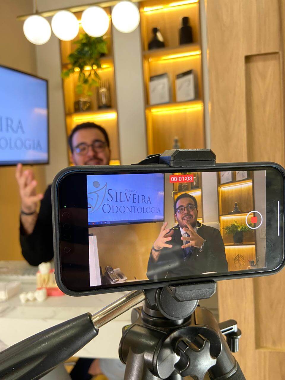 Dr Caio gravano uma aula. Na frente dele o celular em um suporte fazendo a gravação. Dentista no Centro de Franca SP