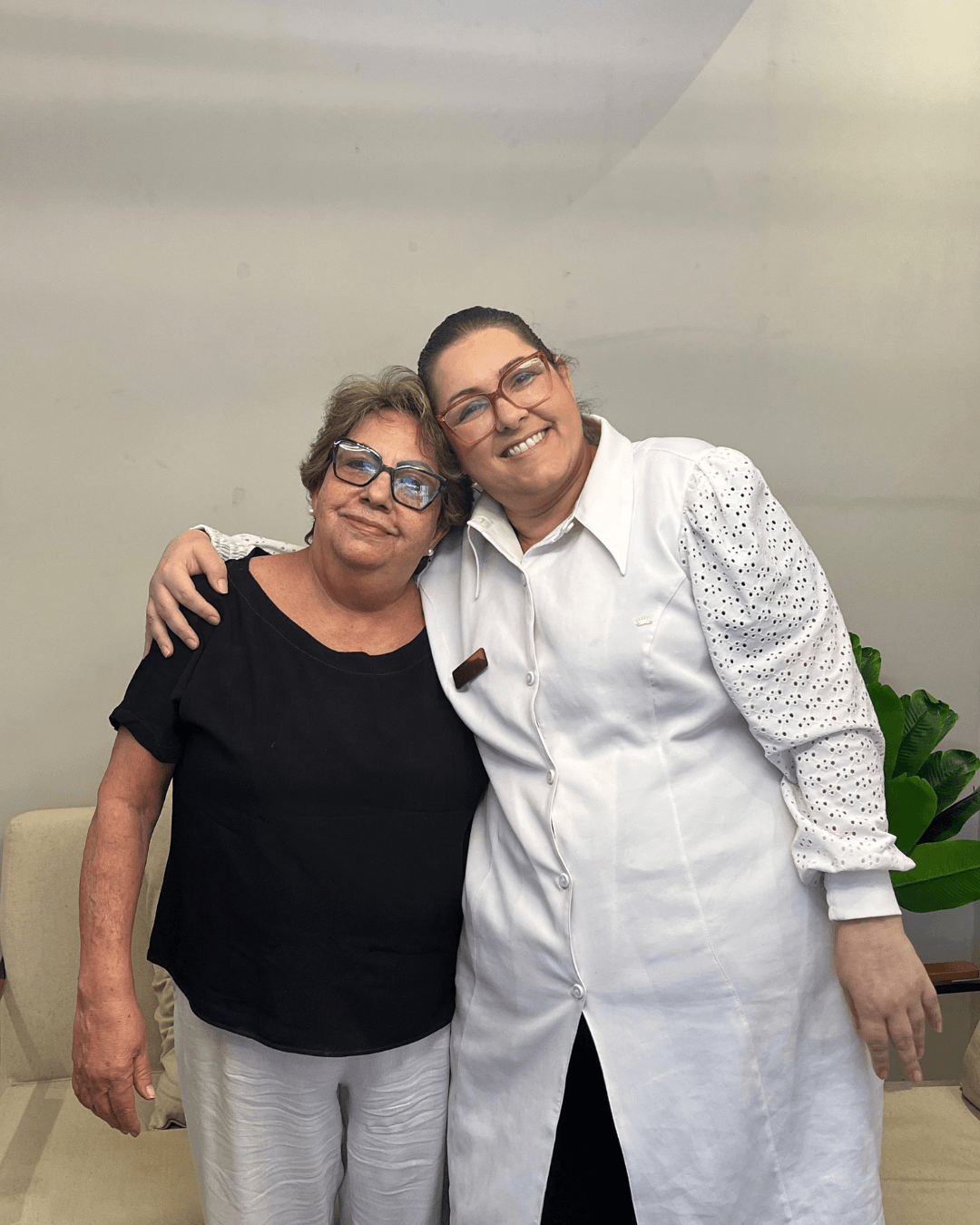 Dentista com jaleco rendado na Silveira Odontologia abraça paciente de óculos celebrando o sucesso dos implantes dentários em Franca SP.