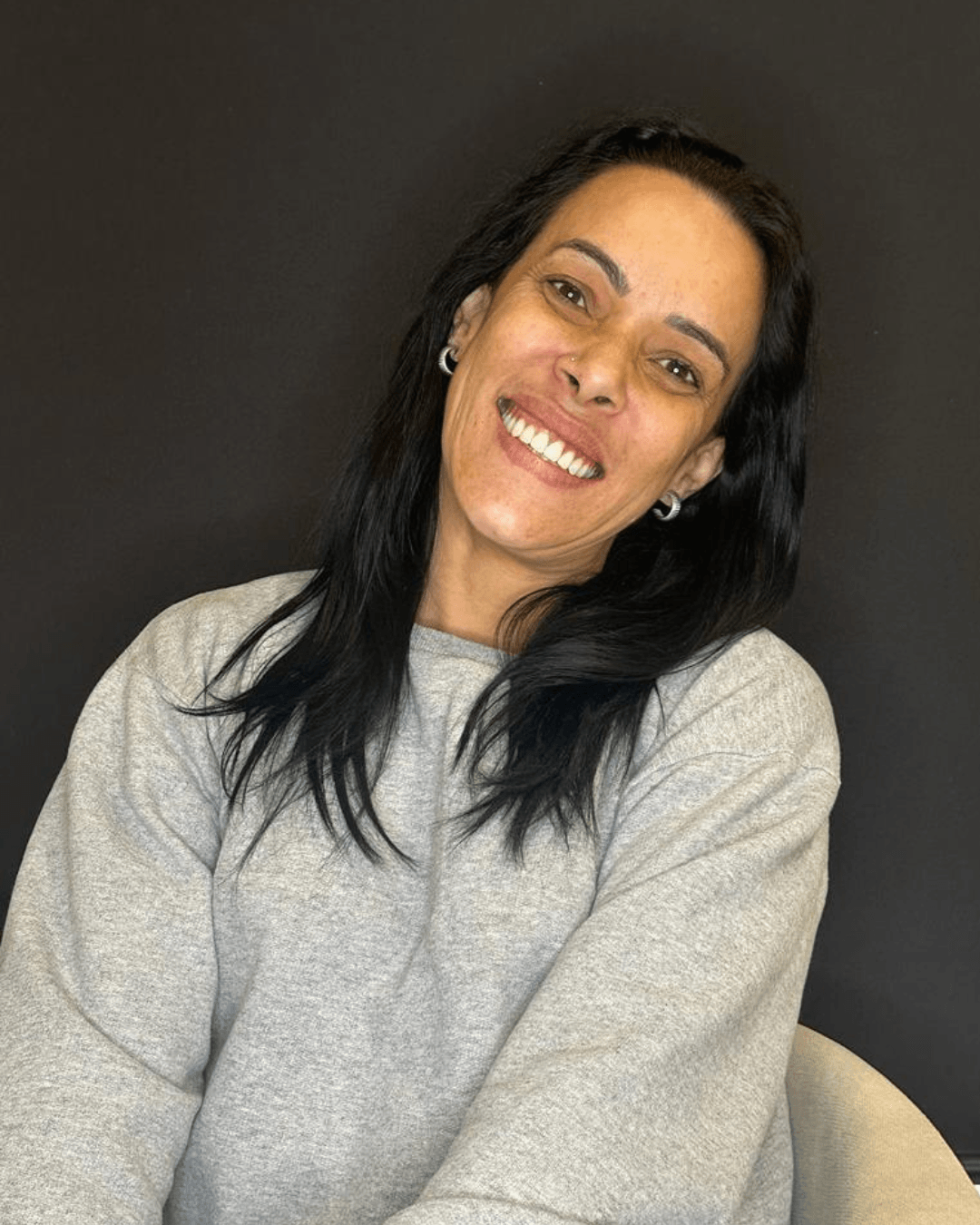 Mulher de cabelos pretos e blusa cinza sorri amplamente exibindo dentes perfeitos reabilitados com prótese protocolo em Franca SP Clínica Geral