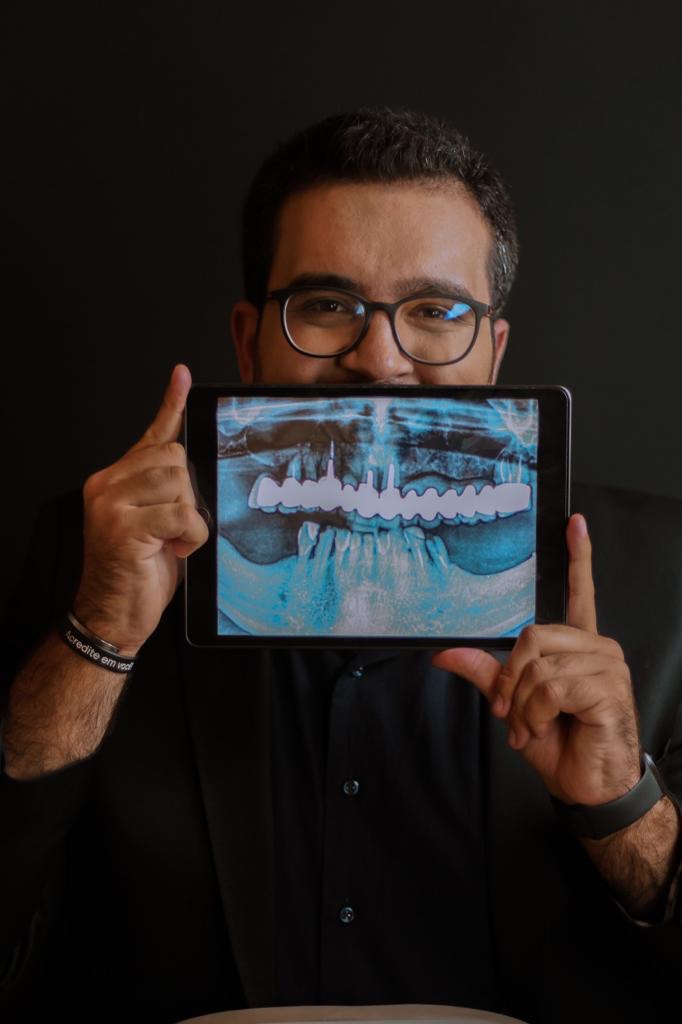 Cirugia Ortognática. Dentista segura tablet mostrando radiografia panorâmica com implantes dentários, destacando o tratamento de reabilitação oral em Franca SP.